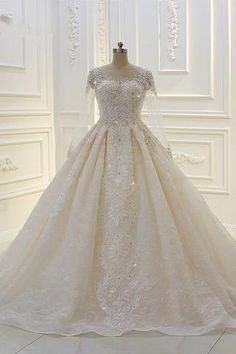 a wedding dress on display in front of a white wall with an intricate lace and beading pattern