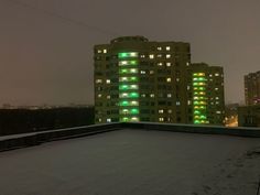 an apartment building is lit up with green lights in the snow at night on a cold winter's day