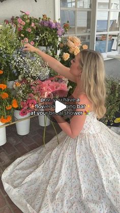 a woman in a white dress picking flowers out of a flower shop with her hand