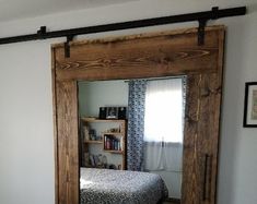 a bed sitting under a mirror next to a wooden framed wall mounted book shelf in a bedroom