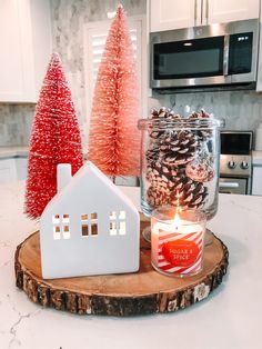 a white house sitting on top of a table next to a lit candle and pine cones