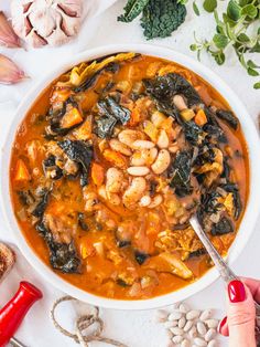 a white bowl filled with shrimp and spinach soup on top of a table next to garlic