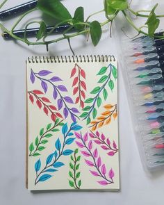 a notebook with colored leaves on it next to some markers and pencils, along with a potted plant