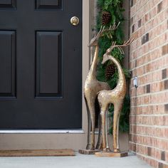 two metal giraffes standing in front of a black door with pine cones on it