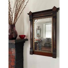 a mirror sitting on top of a mantle next to a vase