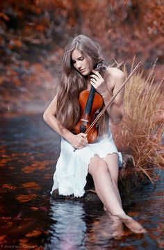 a woman is sitting in the water holding a violin