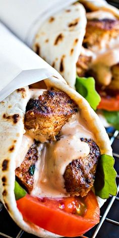 two pita breads with meat, cheese and vegetables wrapped in paper on a cooling rack