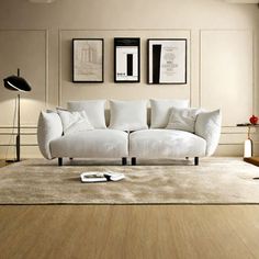 a white couch sitting on top of a wooden floor next to a lamp and pictures