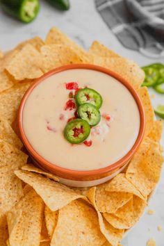 a bowl filled with dip surrounded by tortilla chips and jalapenos