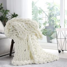 a white blanket sitting on top of a floor next to a chair and potted plant