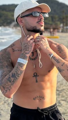 a shirtless man with tattoos on his chest and headphones in his ears stands at the beach