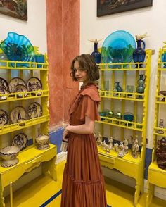 a woman standing in front of yellow shelves filled with vases and other decorative items