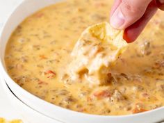 a hand dipping a tortilla chip into a bowl of quesadilla soup