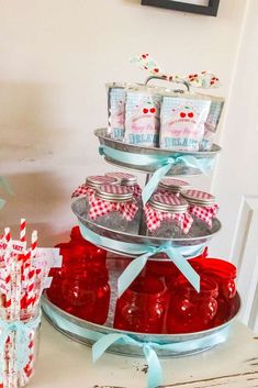 there is a cake stand that has red and white candy jars on it with blue ribbons