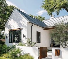 a white house with a metal roof and wooden doors on the front door is surrounded by greenery