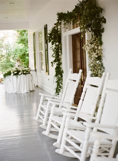 white rocking chairs lined up on the front porch for an outdoor wedding ceremony with flowers and greenery