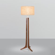 a wooden floor lamp with a beige shade on it's side and a white linen lampshade