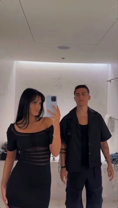 a man standing next to a woman taking a selfie in front of a mirror