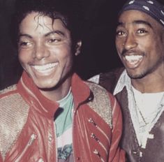 two men are smiling and posing for a photo together, one is wearing a red leather jacket