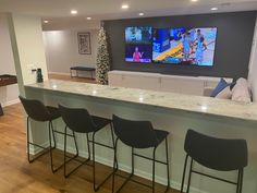 a bar with four stools in front of it and a flat screen tv on the wall