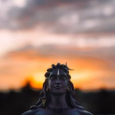 a statue is shown with the sun setting in the back ground behind it and clouds