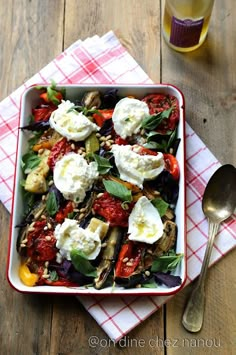 a square bowl filled with vegetables and cheese on top of a red checkered napkin