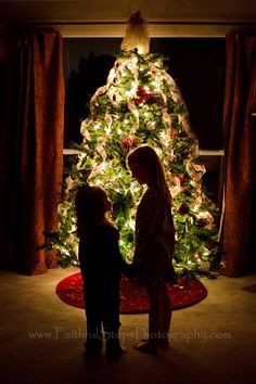 two children standing in front of a christmas tree