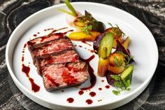 a white plate topped with meat and veggies on top of a marble table