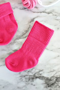 two pink socks sitting on top of a marble counter next to a ball of yarn