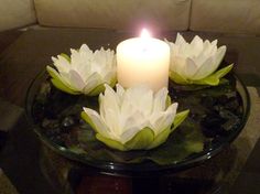 a lit candle sitting on top of a glass bowl filled with water lilies