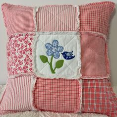 a pink and white quilted pillow with flowers on it's side, sitting on a bed