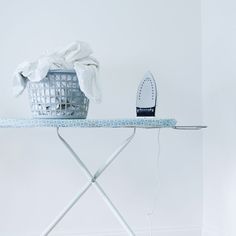 an ironing board sitting on top of a table next to a basket with clothes