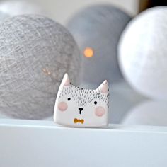 a white cat figurine sitting on top of a table next to balls in the background