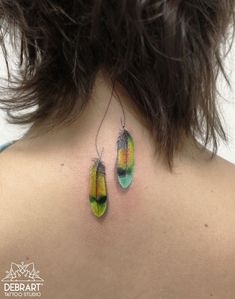 the back of a woman's neck with two colorful earrings on her left side