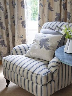 a blue and white chair sitting in front of a window next to a vase with flowers on it