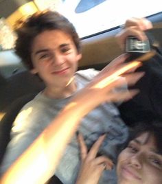 two young men sitting in the back seat of a car, one holding a cell phone