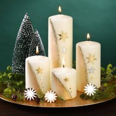 three white candles with gold stars on them and christmas decorations around the candle holders in front of a green background