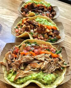 three tacos with meat and veggies on them sitting on a wooden table