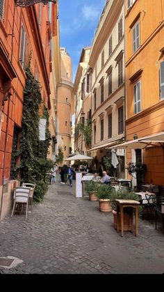 an alley way with tables and chairs on the side, people are walking down it