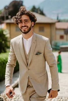 a man in a tan suit and glasses walking down the street with his hand in his pocket