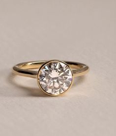 a gold ring with a white diamond in the center on a plain surface that is light gray