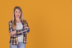 a woman standing with her arms crossed in front of an orange background and looking at the camera