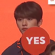 the young man is holding up a red sign with yes written on it in front of an orange background