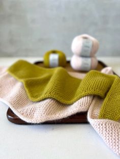 a knitted blanket and two balls of yarn sitting on a wooden stand next to each other