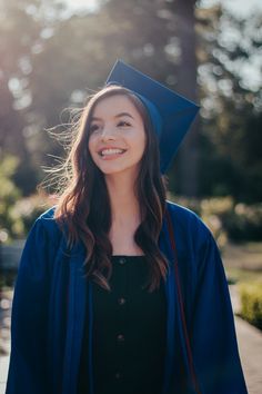 a woman wearing a blue graduation cap and gown smiles at the camera while standing outside