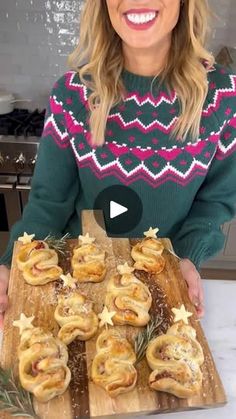 a woman holding a wooden cutting board with pastries on it