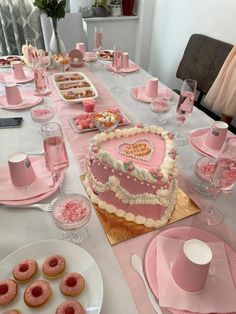 a heart shaped cake sitting on top of a table next to pink plates and cups