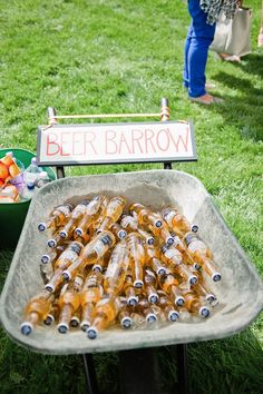 there are many bottles of beer in the wheelbarrow on the grass next to a sign that says beer barrow