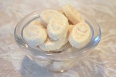 a glass bowl filled with sugared donuts on top of a lace tablecloth