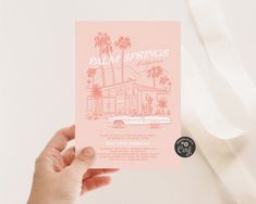 a person holding up a pink card with palm trees on it and the words palm springs written in white